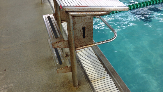 a stainless steel Paddock starting block, covered in rust from chloramines, next to a swimming pool